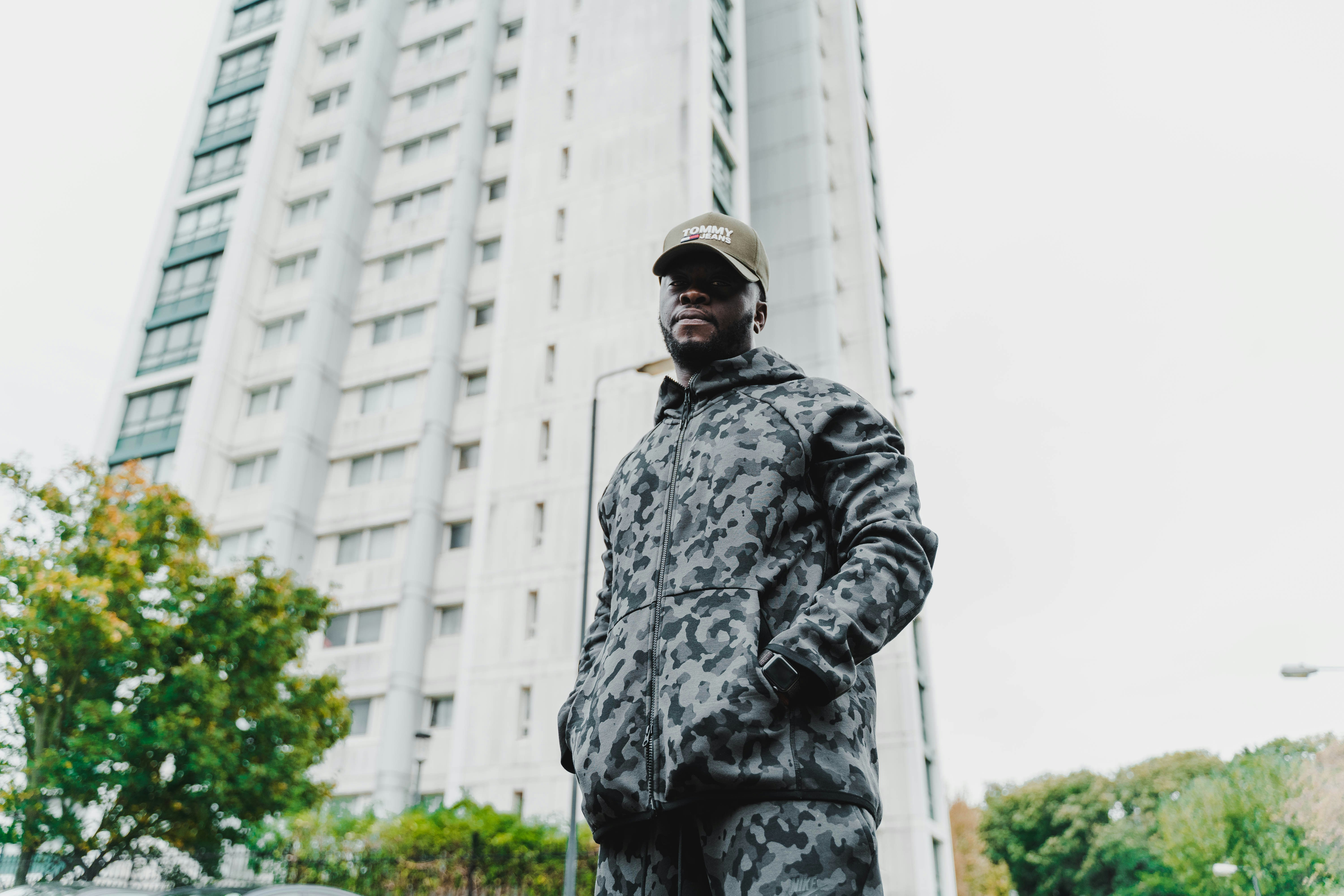 man in black and grey camouflage jacket standing near white concrete building during daytime