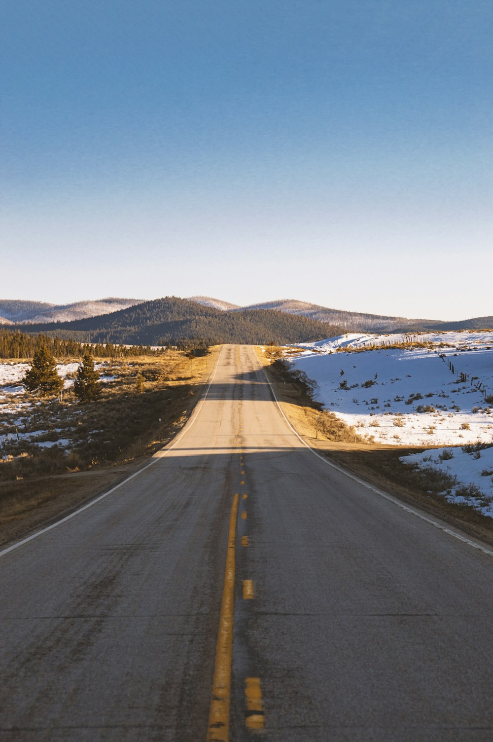 gray asphalt road near snow covered field during daytime