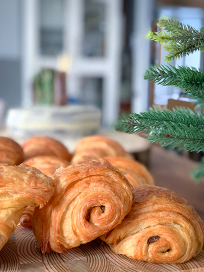 Hands gently placing freshly baked pastries into a warm brown parchment-lined box, set against a cozy cream background.