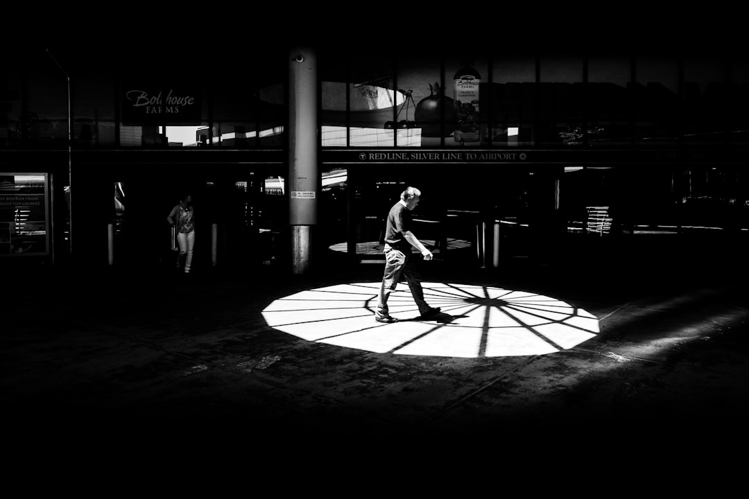 grayscale photo of man in white shirt and black pants walking on street