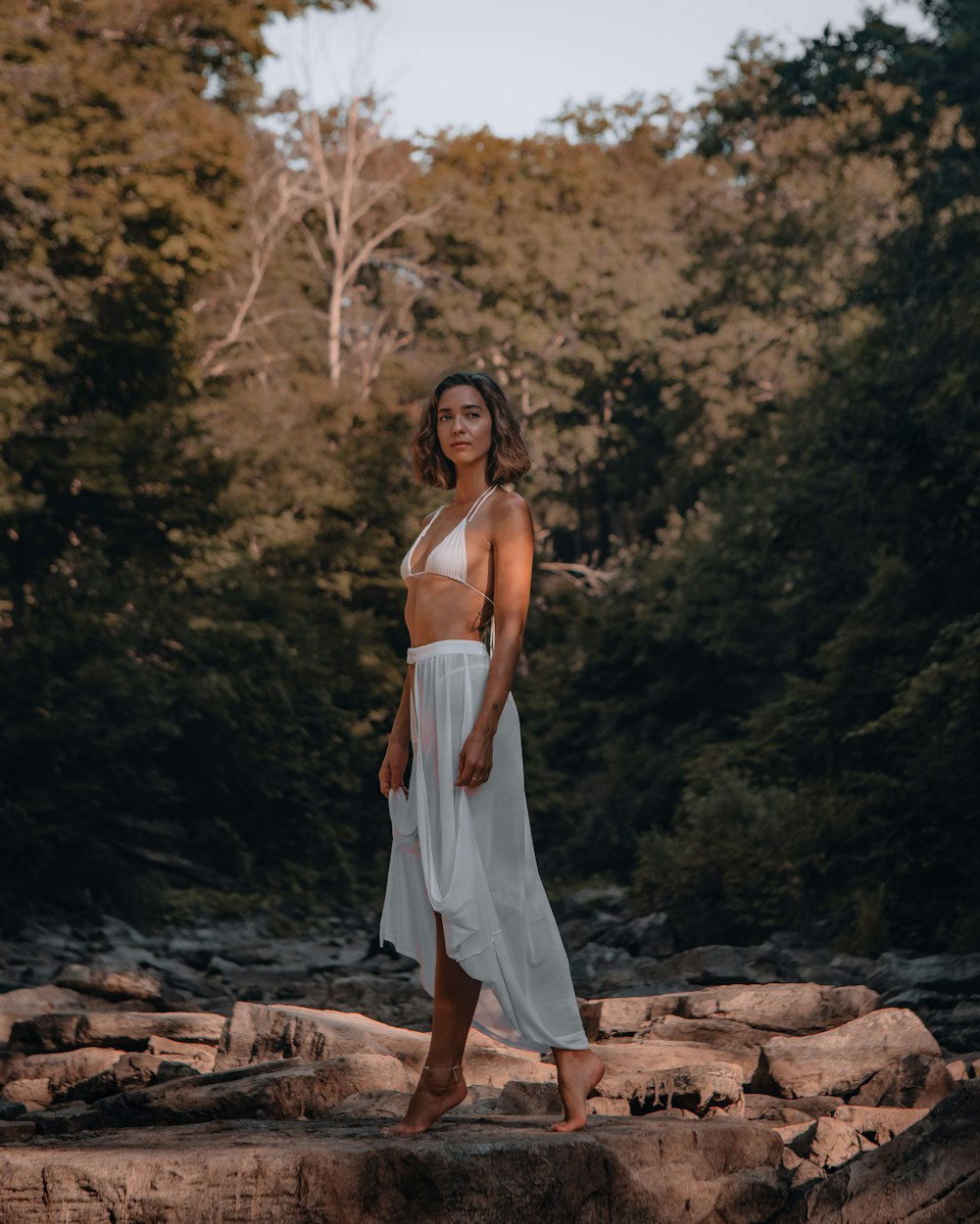 woman in white spaghetti strap dress standing on brown rock during daytime