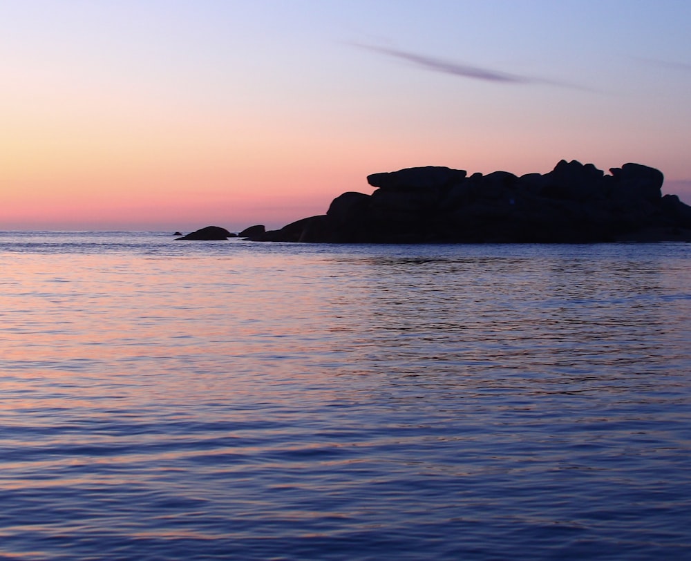 silhouette of rock formation on sea during sunset