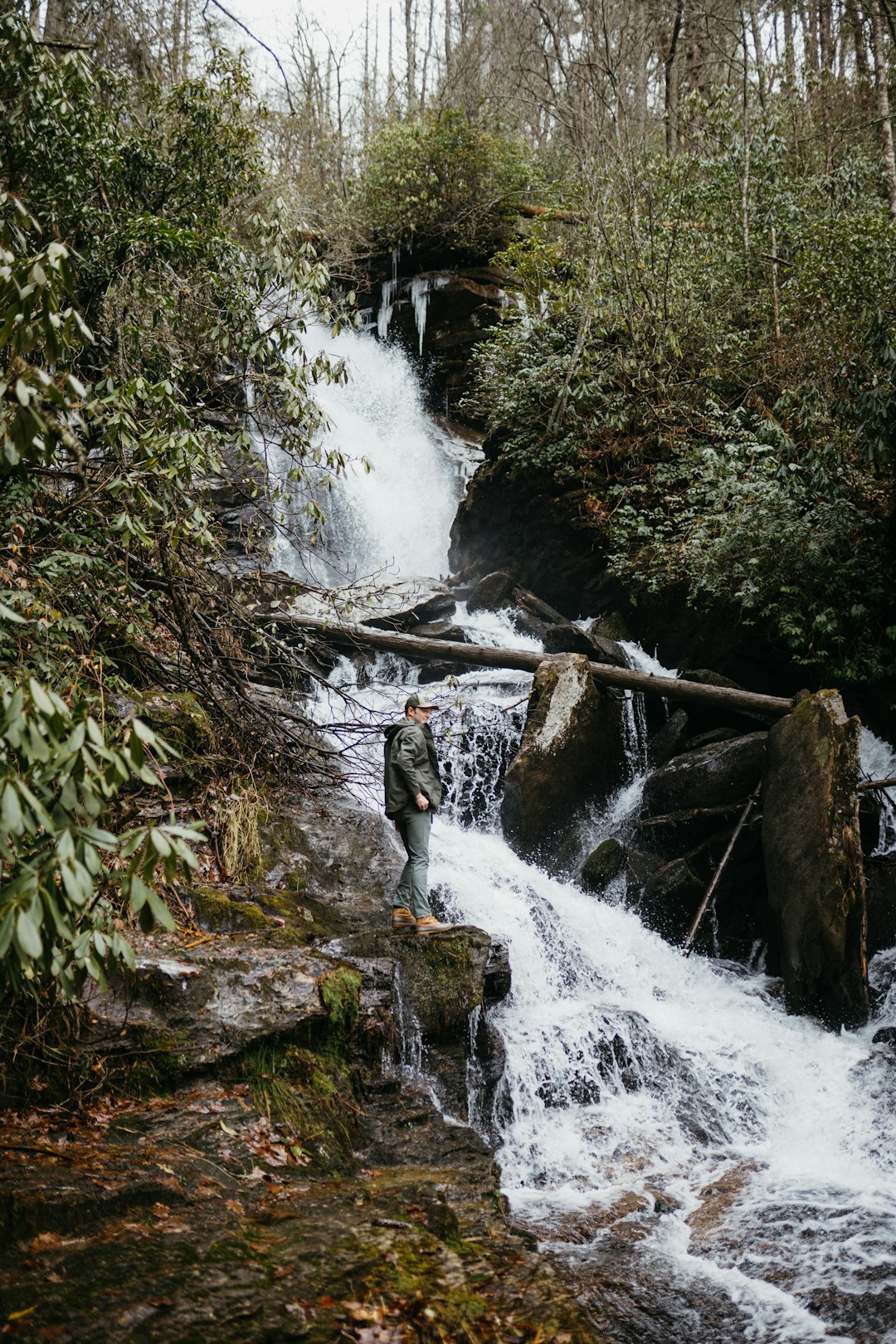 person in black pants standing on rock near waterfalls during daytime