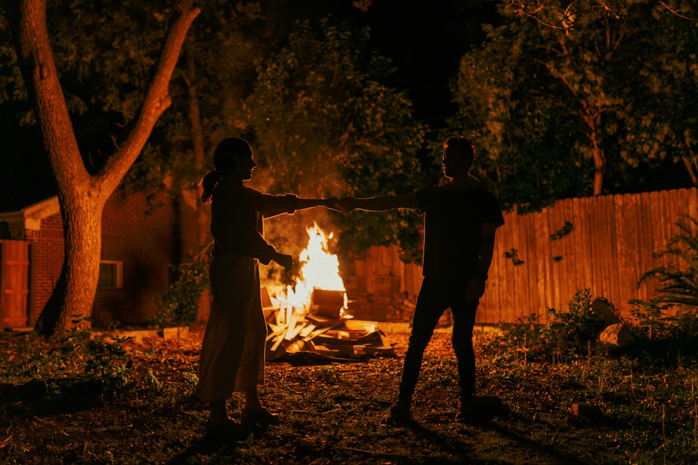 silhouette of 2 men standing near bonfire during night time