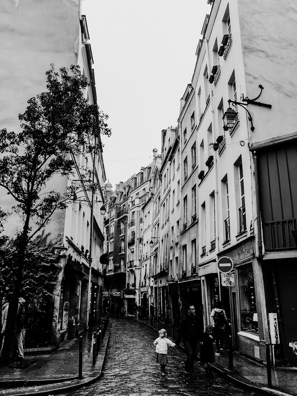 grayscale photo of people walking on street between buildings