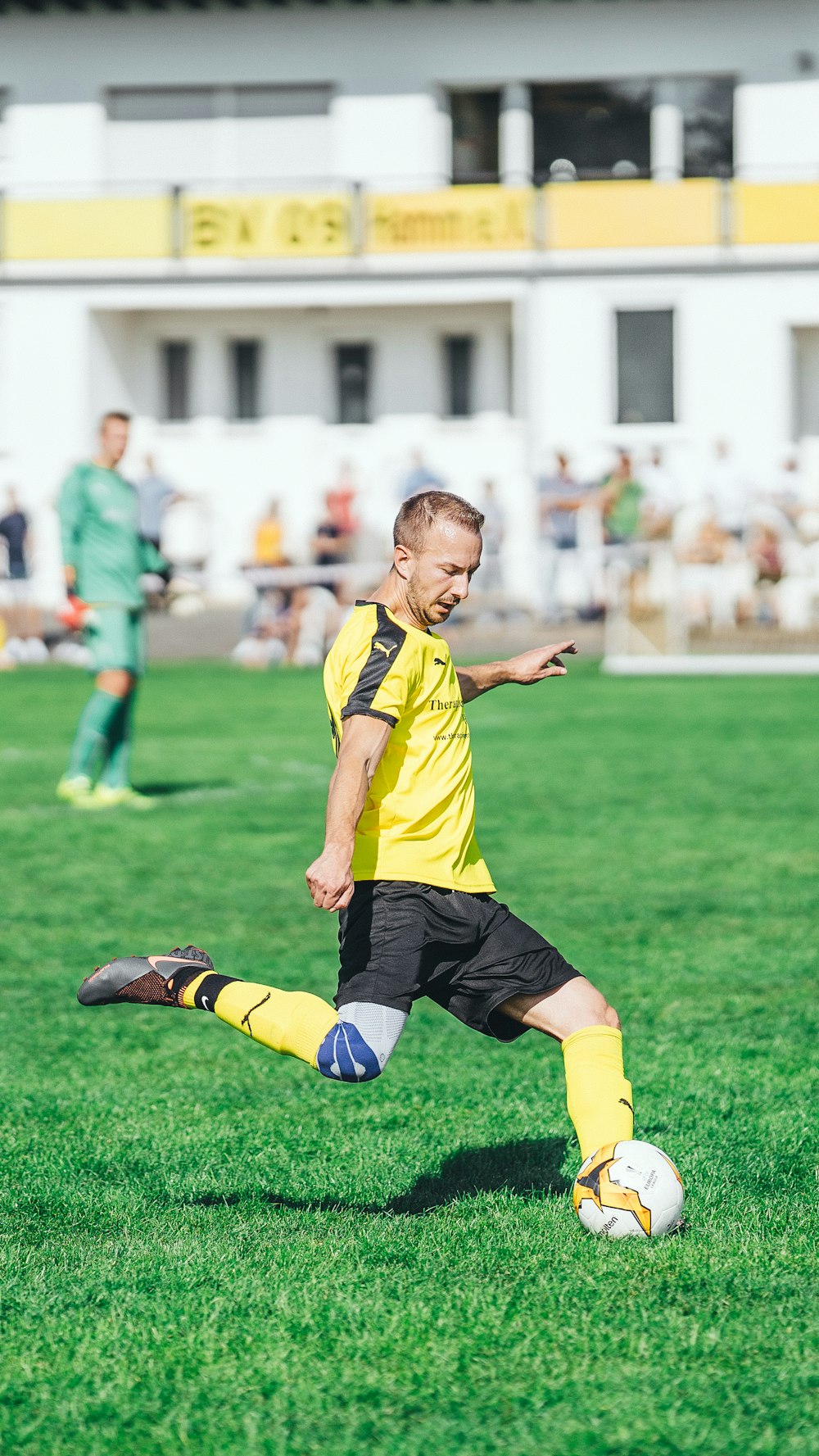 Junge im gelb-schwarzen Fußballtrikot kickt tagsüber Fußball auf grünem Rasen