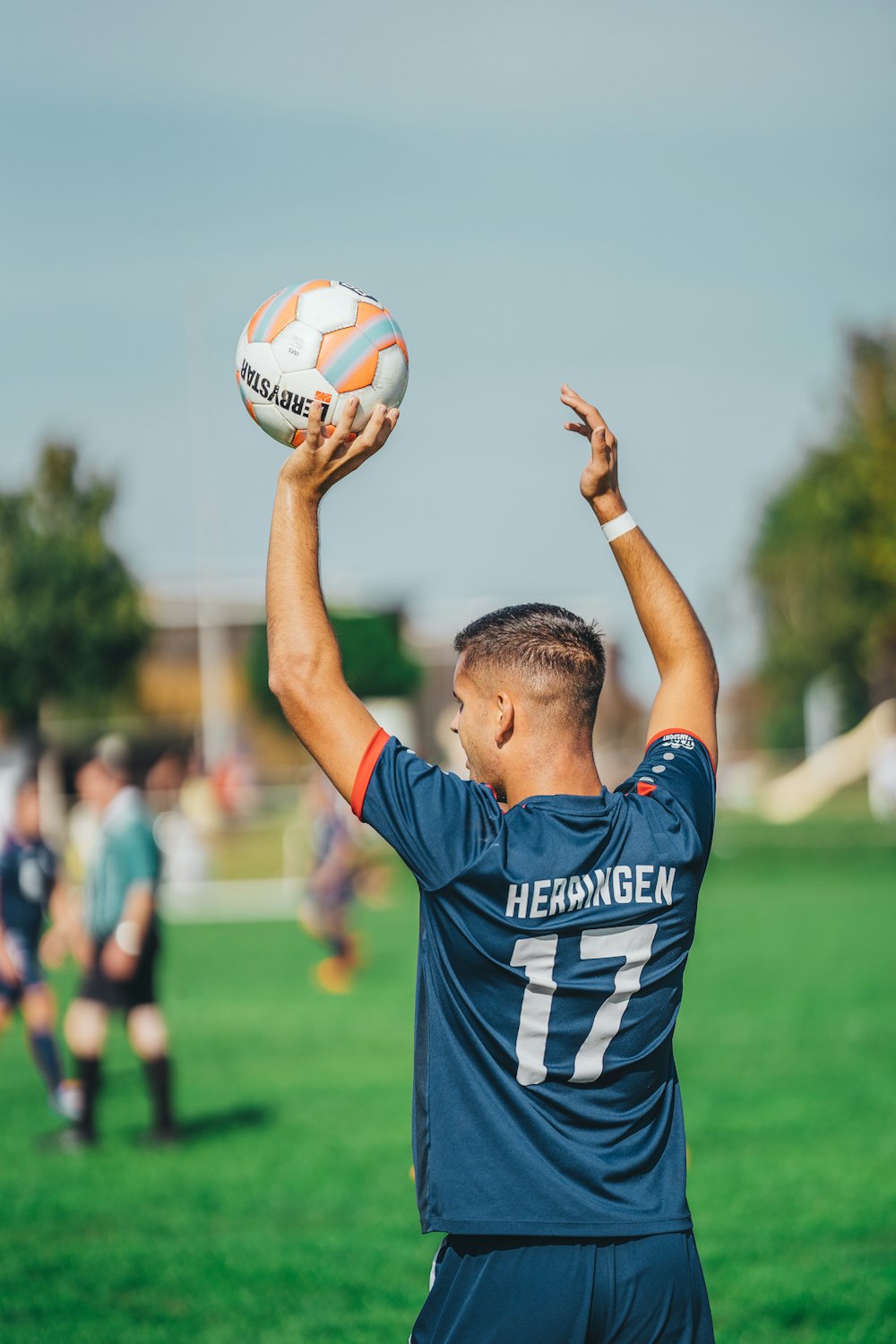 青と白のアディダスサッカージャージシャツを着た男が白と青のサッカーボールを持っている