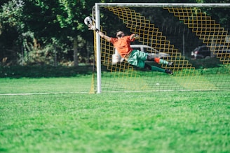 man in red shirt and black pants playing soccer during daytime