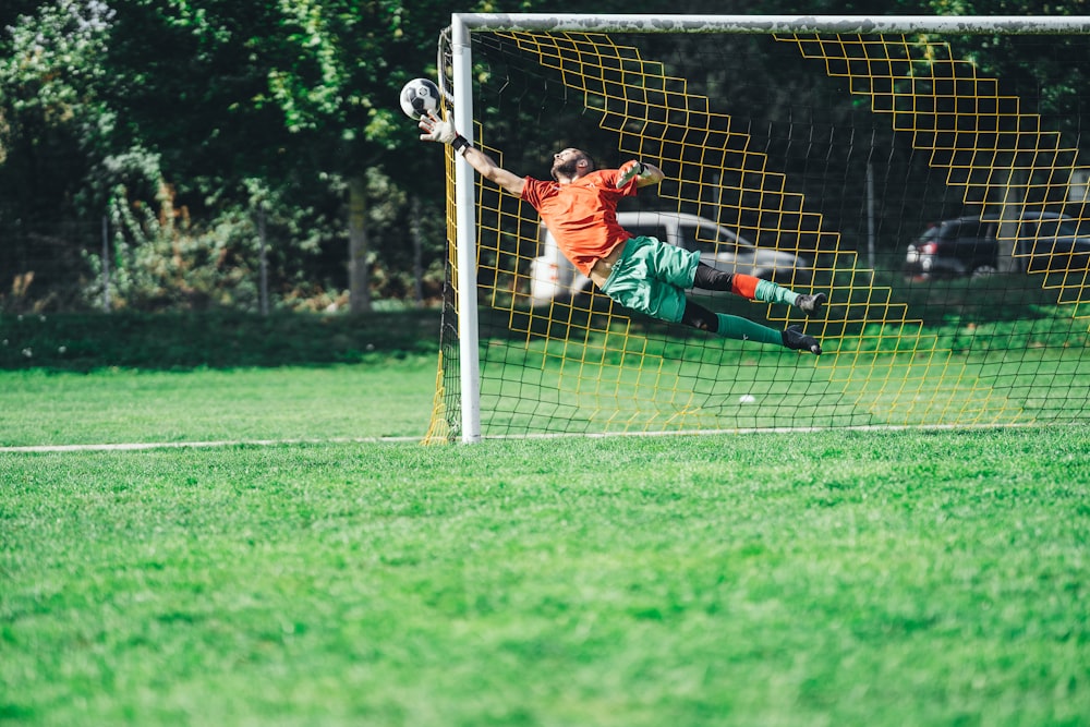 man in red shirt and black pants playing soccer during daytime