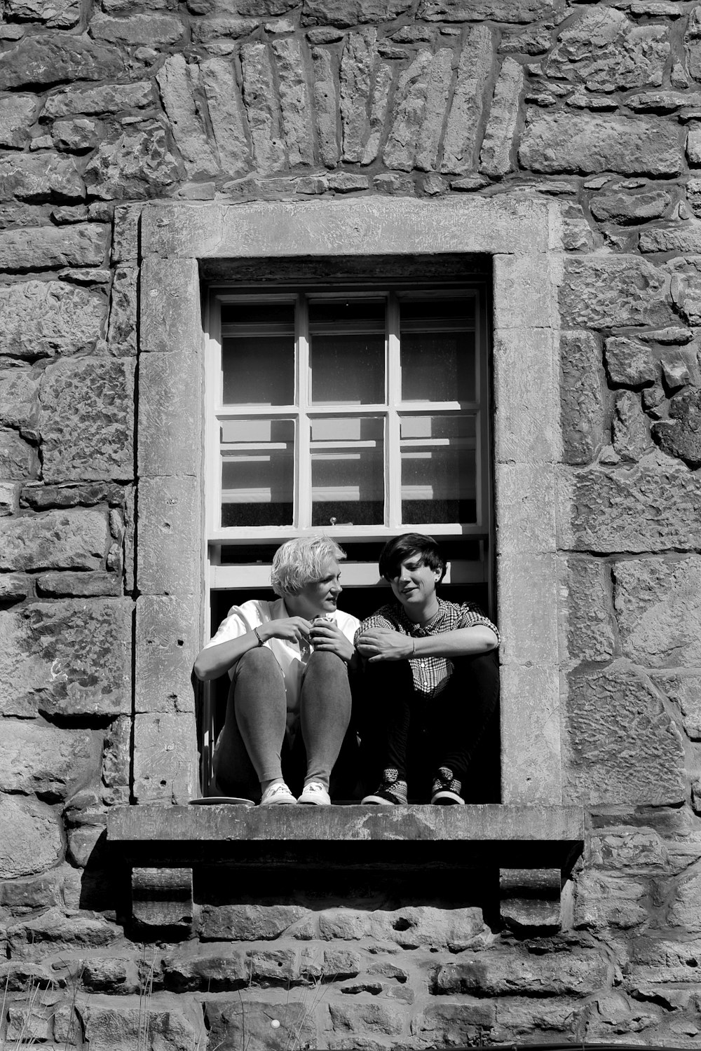 grayscale photo of 2 women sitting on window