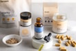 A collection of wellness products is displayed, including a brown glass dropper bottle with a blue label, jars with cream-colored labels, a small bowl with powder, and several capsules scattered on a light surface. Packaging with minimalist design features the brand 'beam' and labels such as 'clarity,' 'the fixer,' and 'revive.'