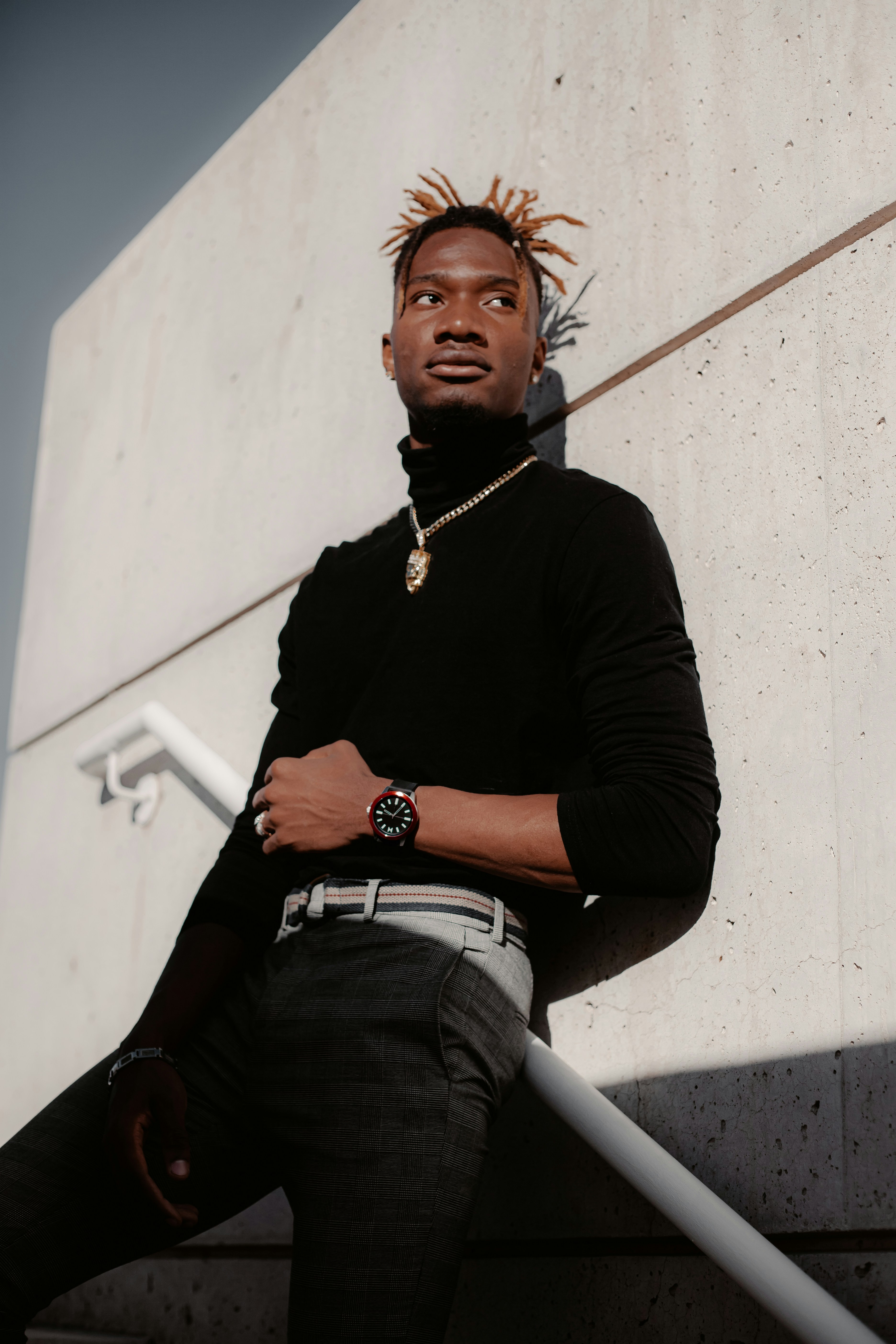 白いコンクリートの壁に座る黒い長袖シャツとブルーデニムジーンズの男