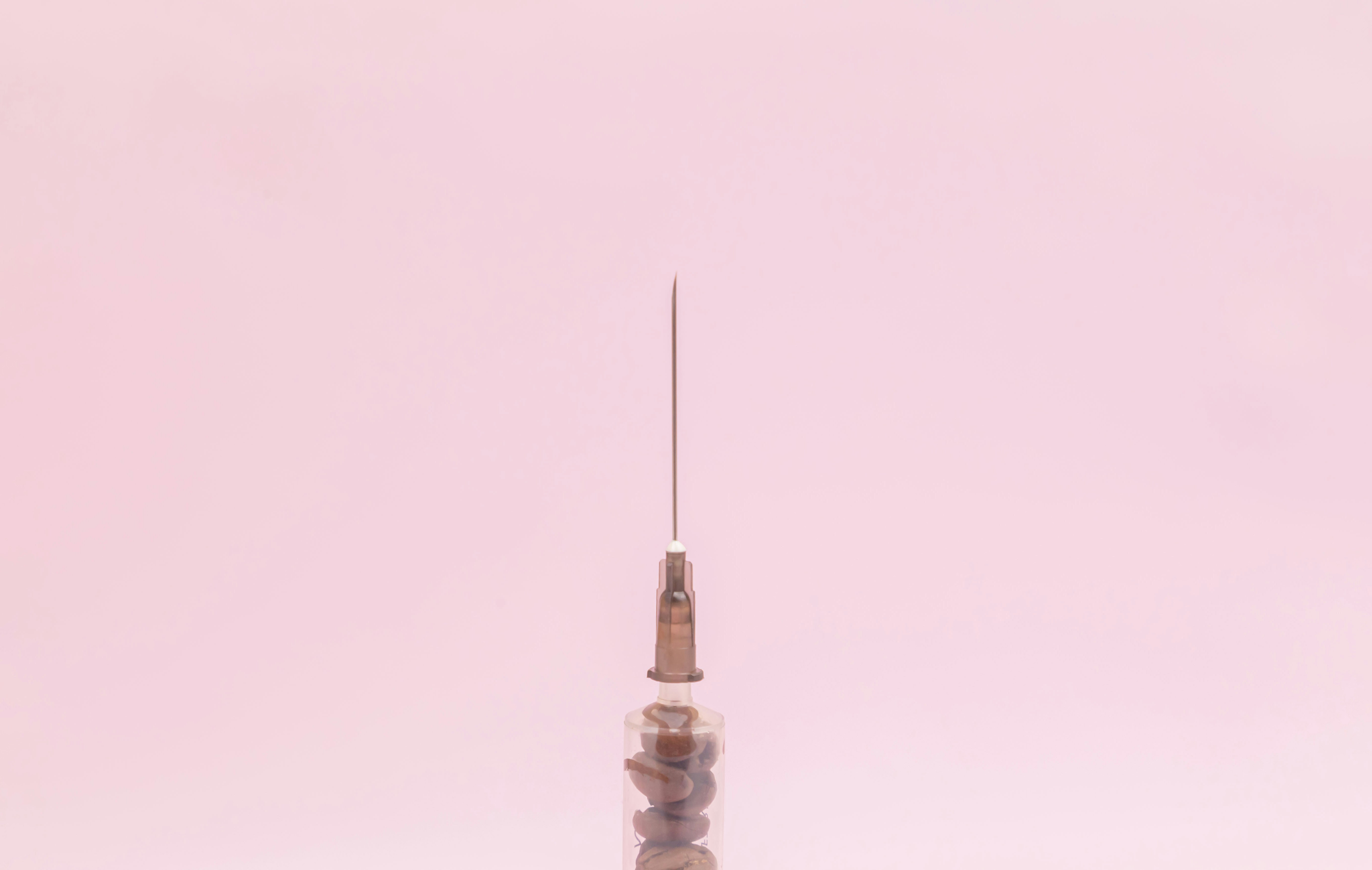 Transparent syringe with coffee beans inside on a pink background. View from above. Advertising. Place for an inscription. The medicine. Coffee. Intravenous coffee. Syringe. Kofenin. Energy.