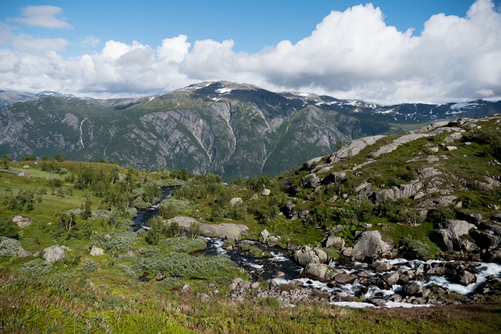 green grass field near mountain under white clouds during daytime