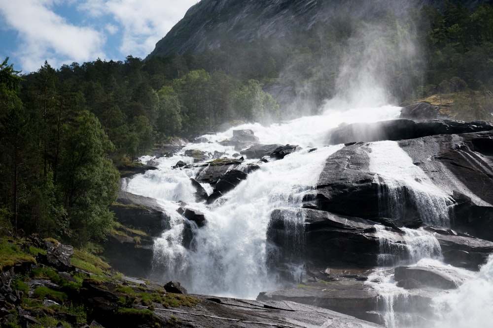 water falls on rocky mountain under blue sky during daytime