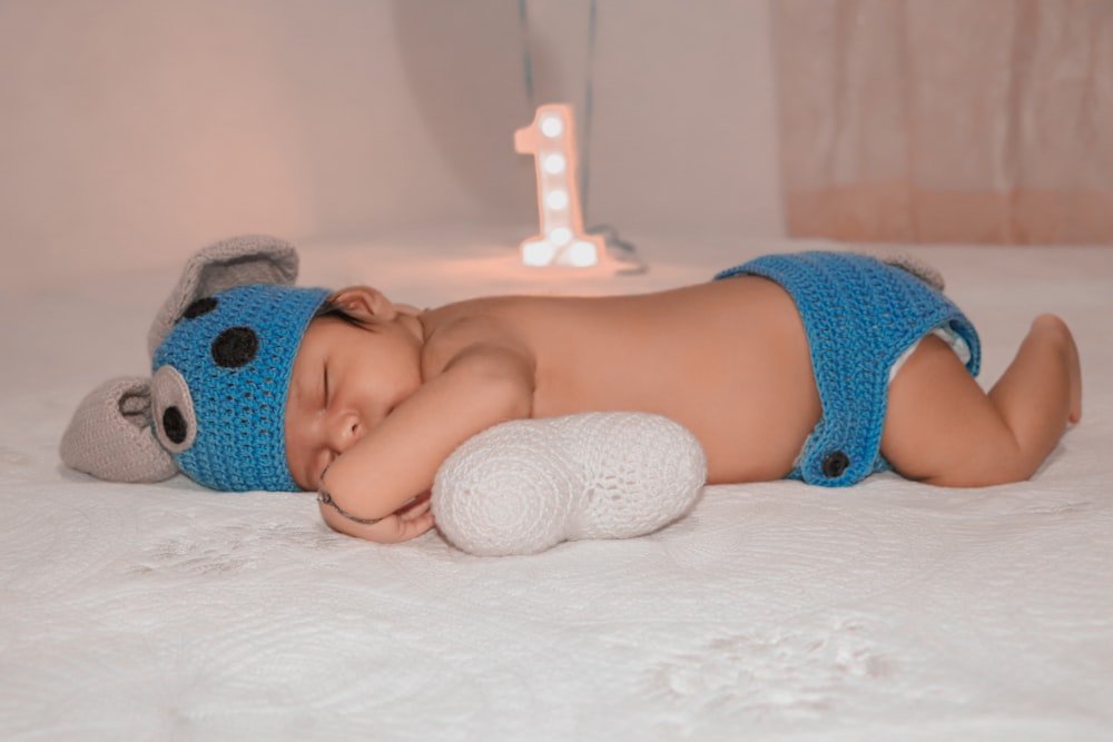 baby in blue and white polka dot knit cap lying on bed