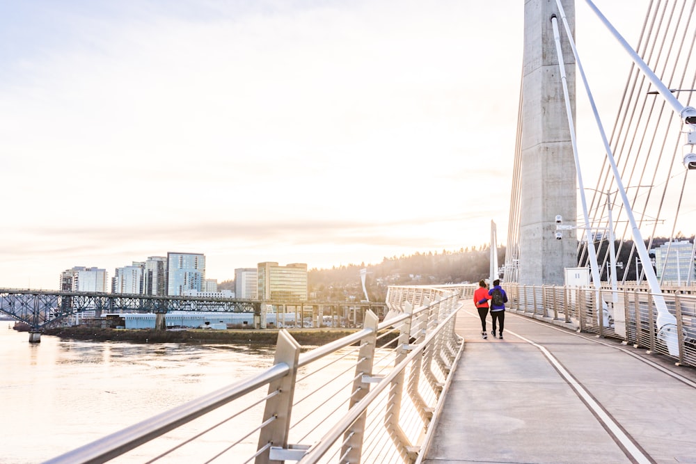 man in red jacket and blue denim jeans walking on gray concrete bridge during daytime