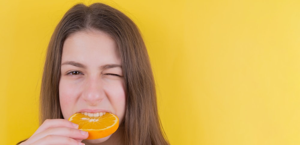 menina que segura a fruta laranja na frente da parede amarela