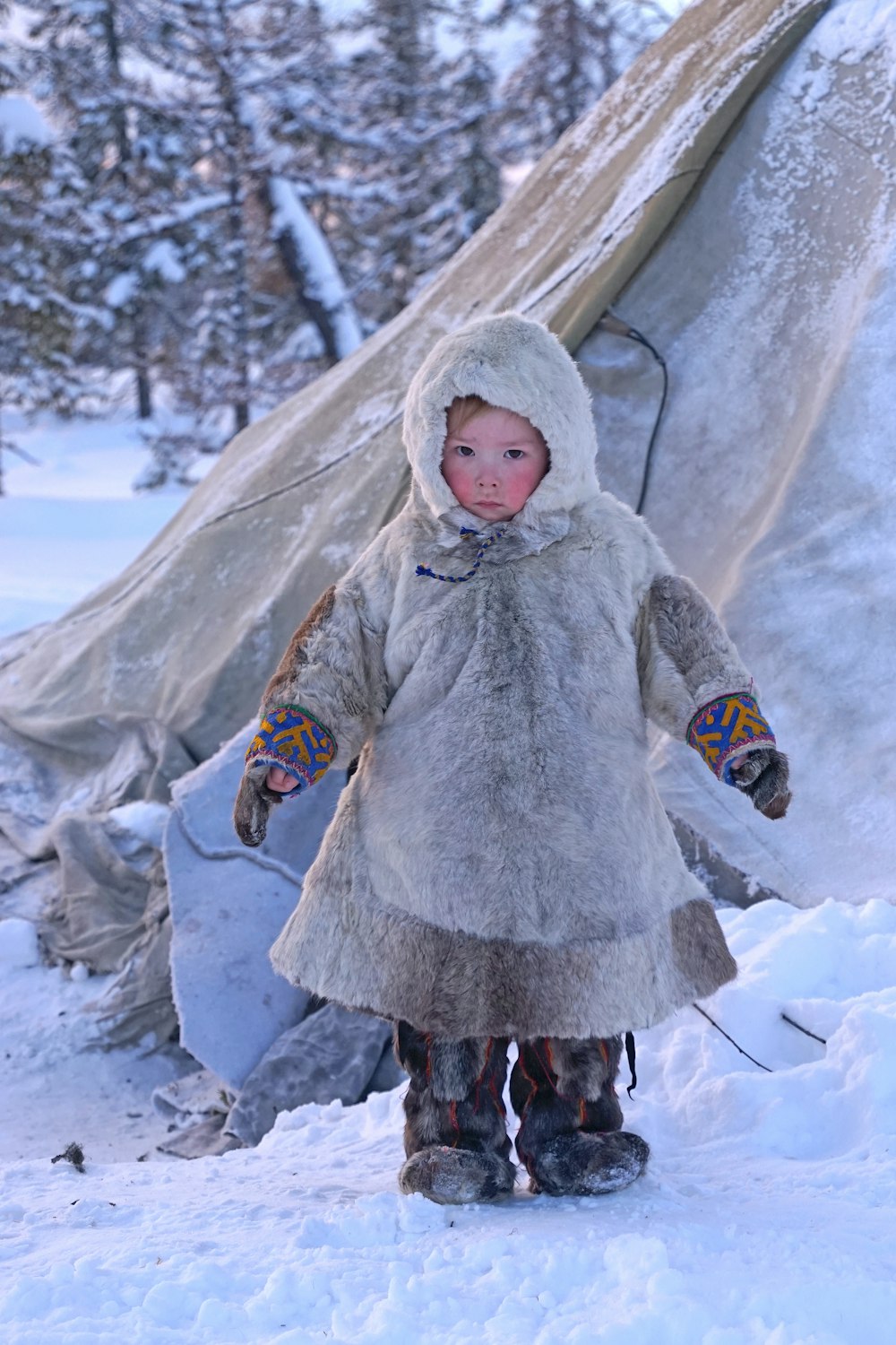 昼間、雪に覆われた地面に立つ灰色のコートの少女
