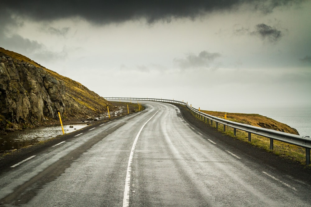 gray concrete road between brown grass field under gray sky