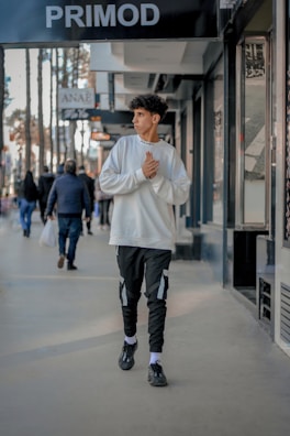 Man walking through a city street in a charcoal sweatshirt featuring a minimalist cross graphic.