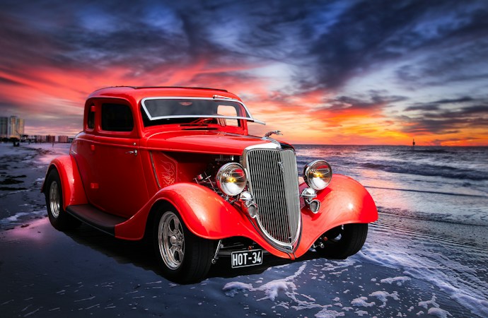 A red classic car with polished chrome parked on a street during a downtown car show