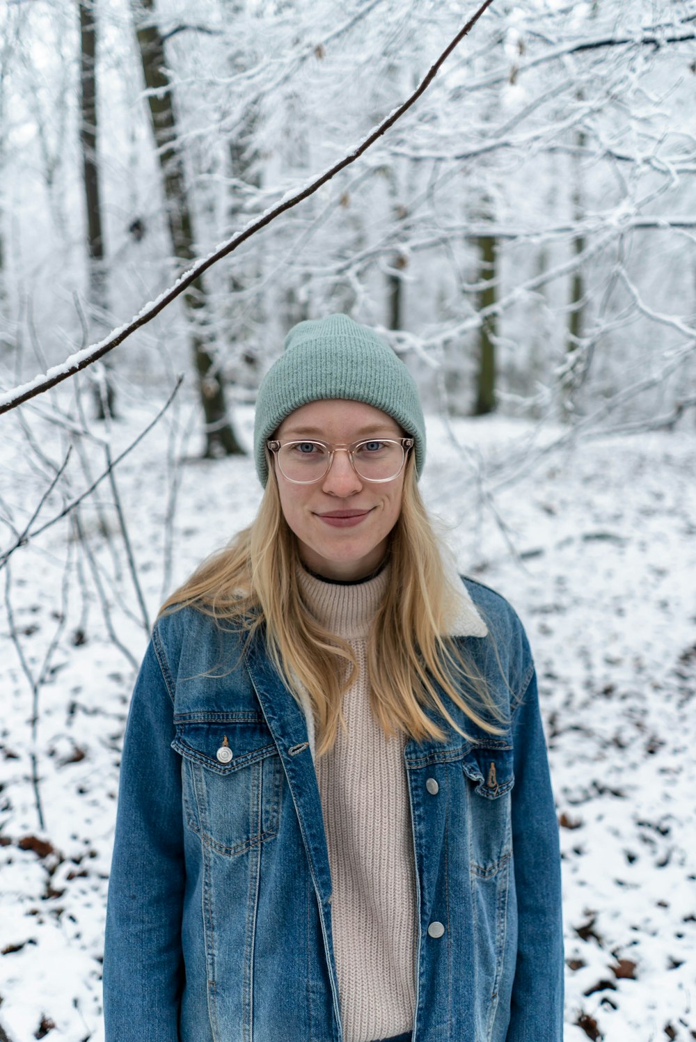 woman in blue denim jacket and green knit cap standing on snow covered ground during daytime