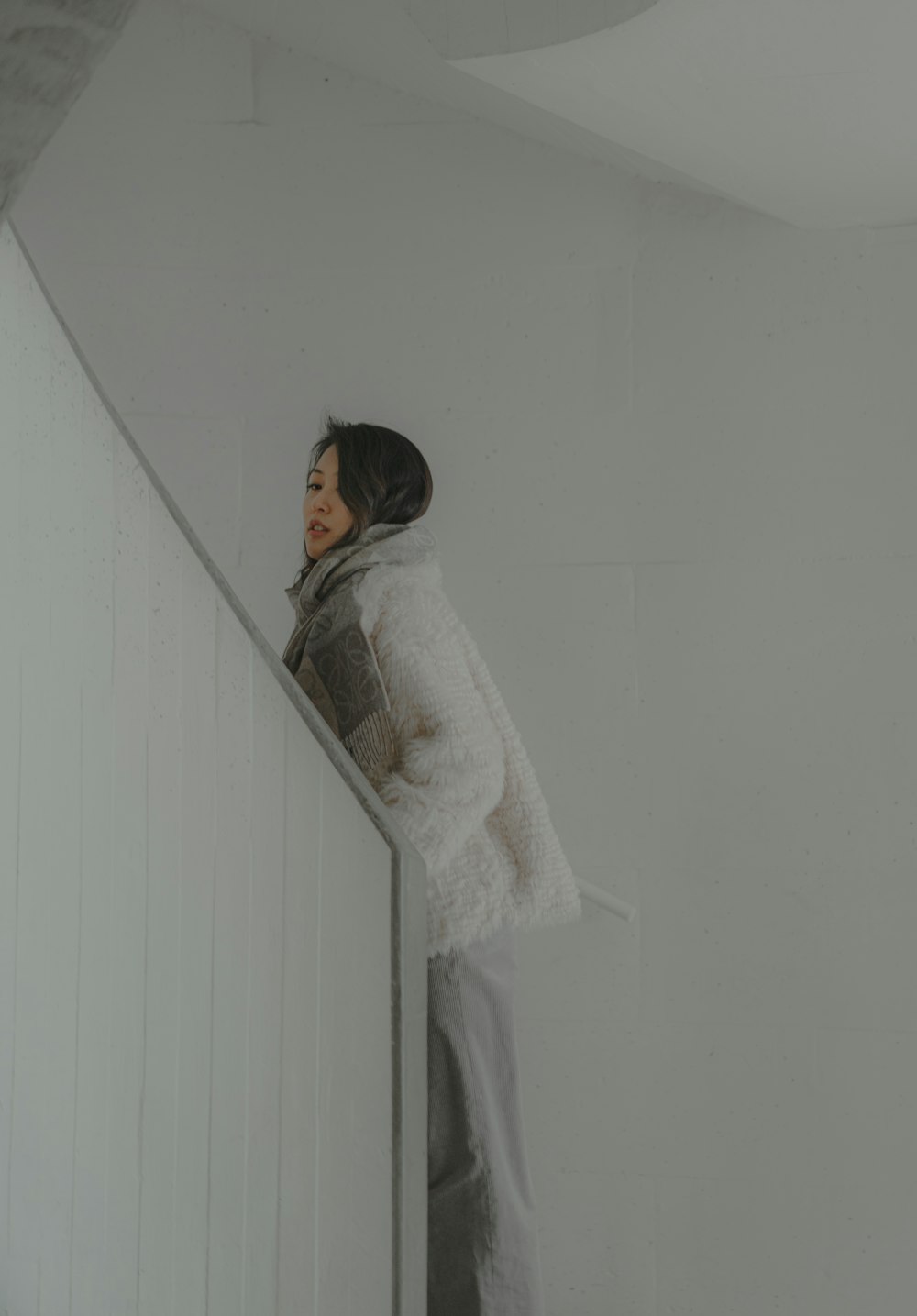 woman in white fur coat leaning on white wall