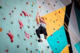 A person is climbing an indoor rock wall, which is equipped with colorful holds of various shapes and sizes. The climber is wearing a harness and appears to be mid-climb, showcasing determination and focus.