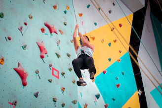 A climber gripping colorful holds on an indoor rock wall, focused and determined.
