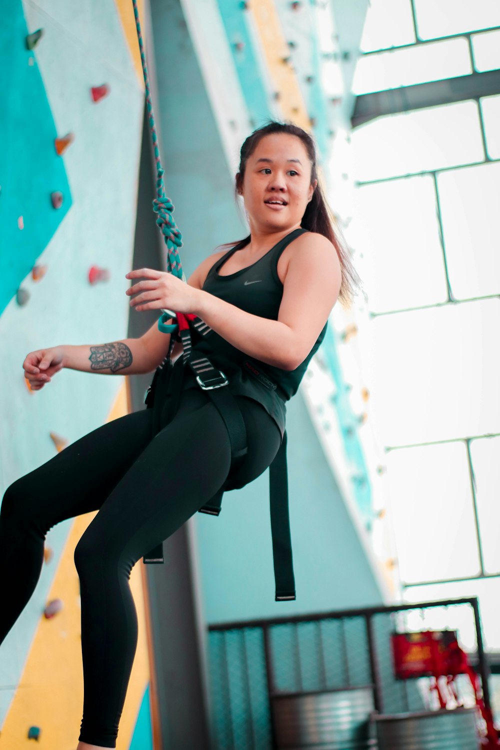 Femme en débardeur noir et leggings noirs assis sur un mur de béton blanc pendant la journée