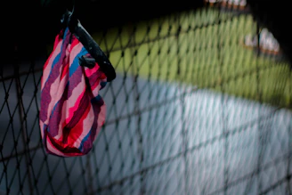 A vibrant red backpack hanging on a rustic fence with a sunny field in the background.