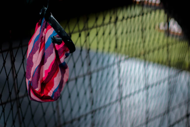 A vibrant red backpack hanging on a rustic fence with a sunny field in the background.