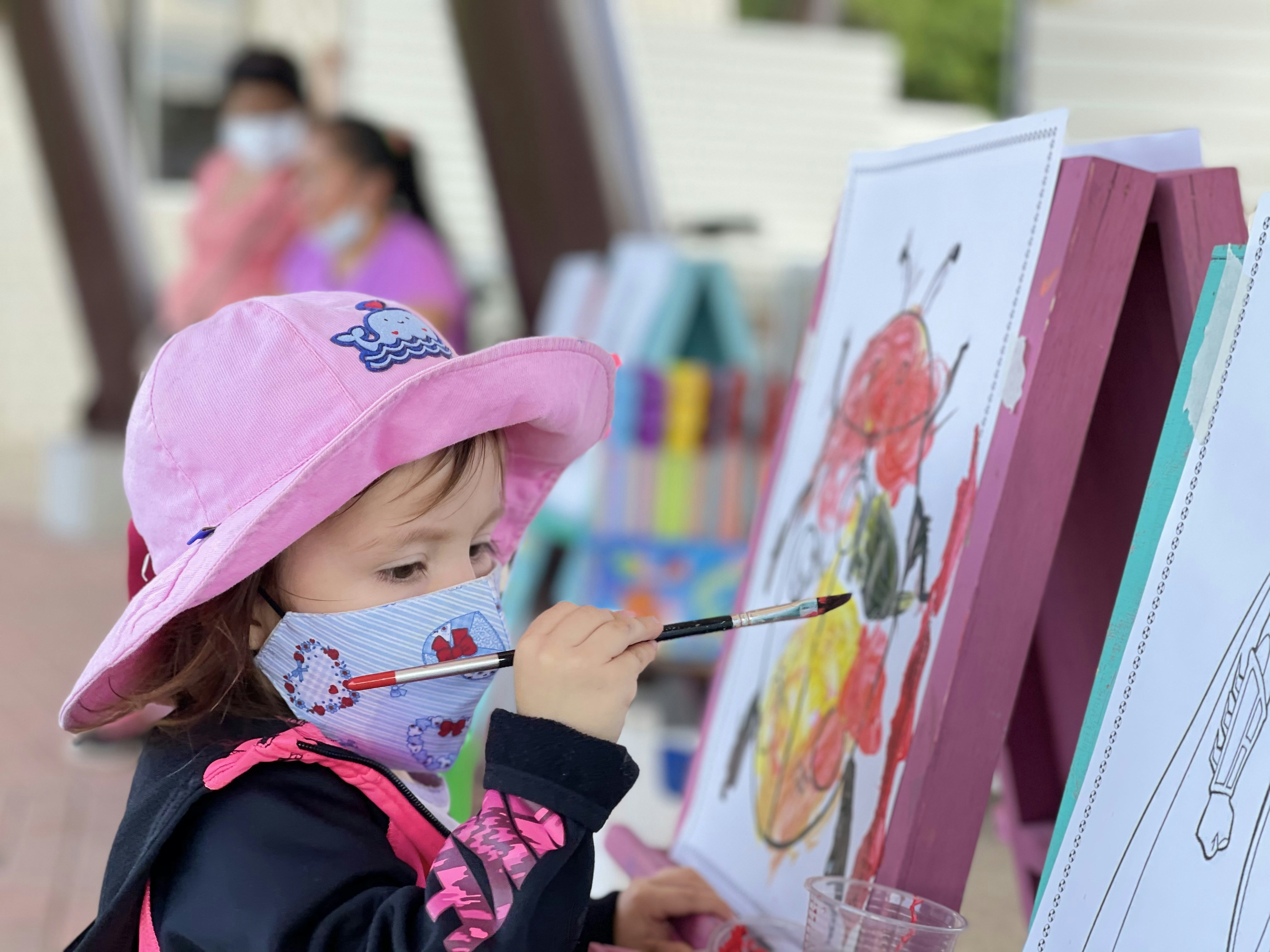 girl in pink cap and black jacket painting on white board