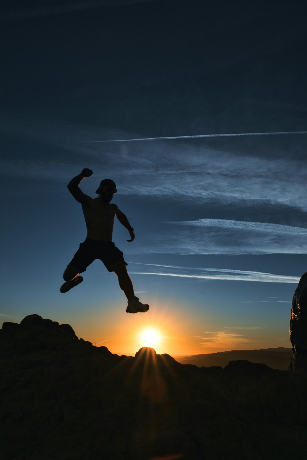 Silueta del hombre saltando sobre la roca durante la puesta del sol