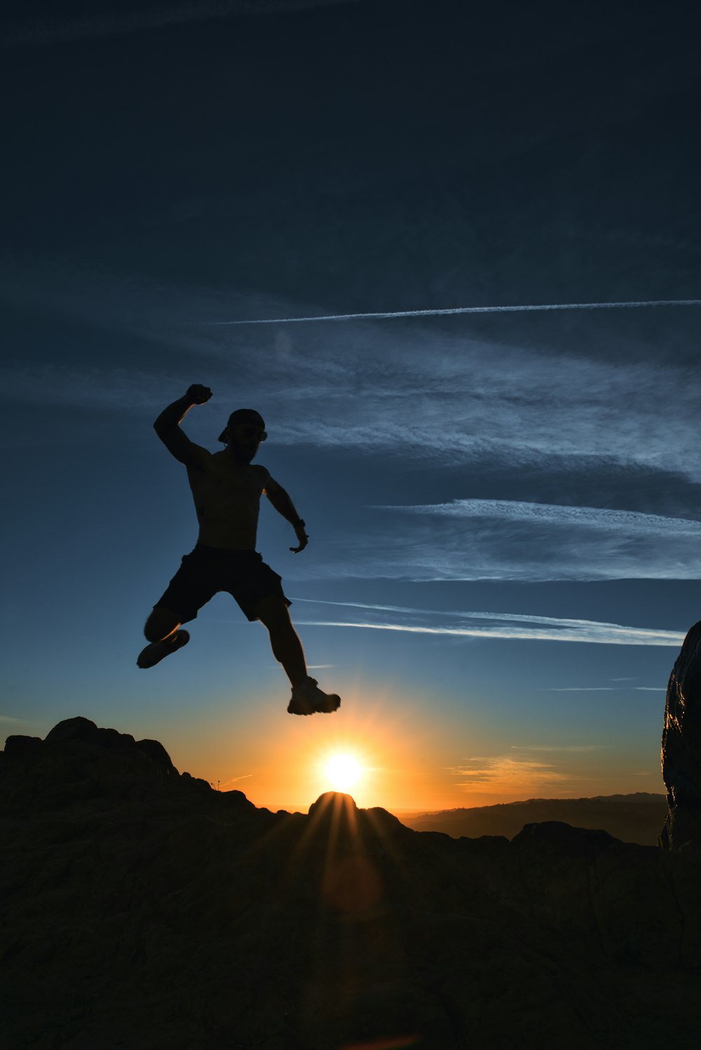 silhouette of man jumping on rock during sunset