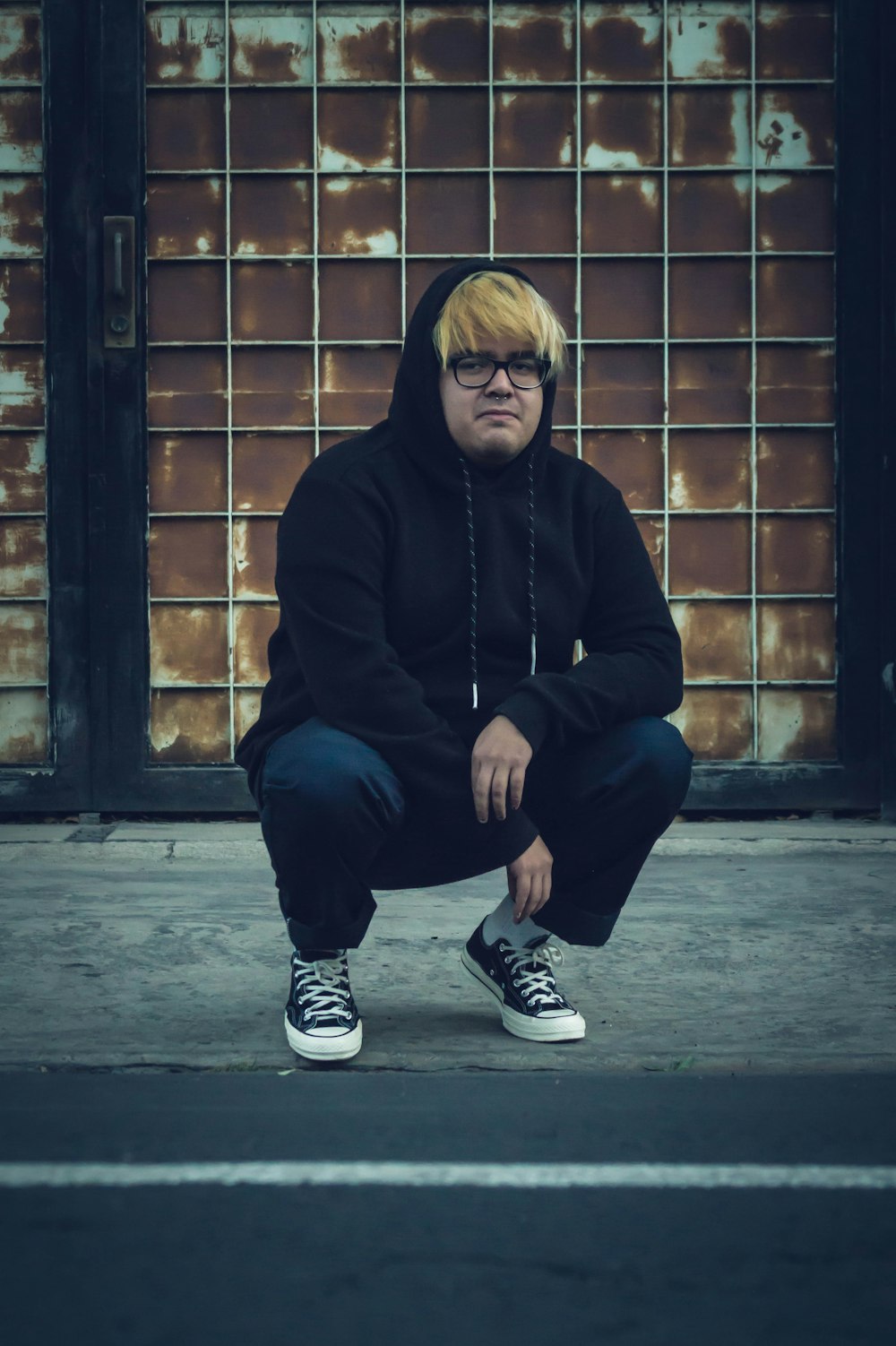 man in black hoodie and blue denim jeans sitting on brown brick wall