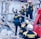 Rescue workers wearing helmets and uniforms are navigating a scene of destruction, likely from a collapsed building. They are surrounded by rubble and debris as they communicate and coordinate the rescue efforts.