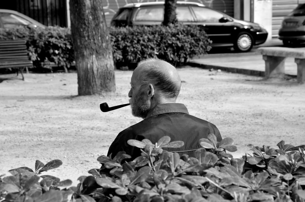 grayscale photo of man in jacket sitting on ground with dried leaves