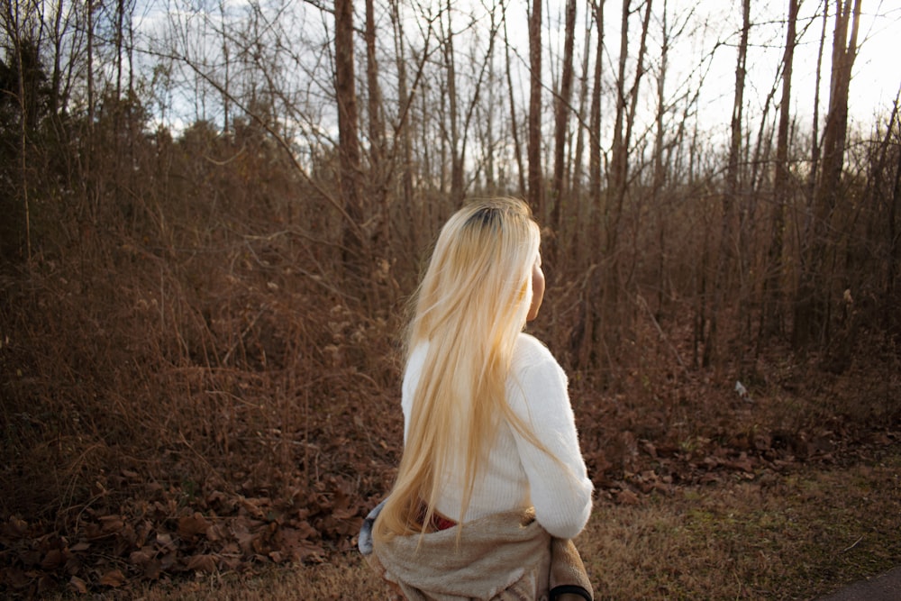 Femme en chemise blanche à manches longues debout sur le champ d’herbe brune pendant la journée
