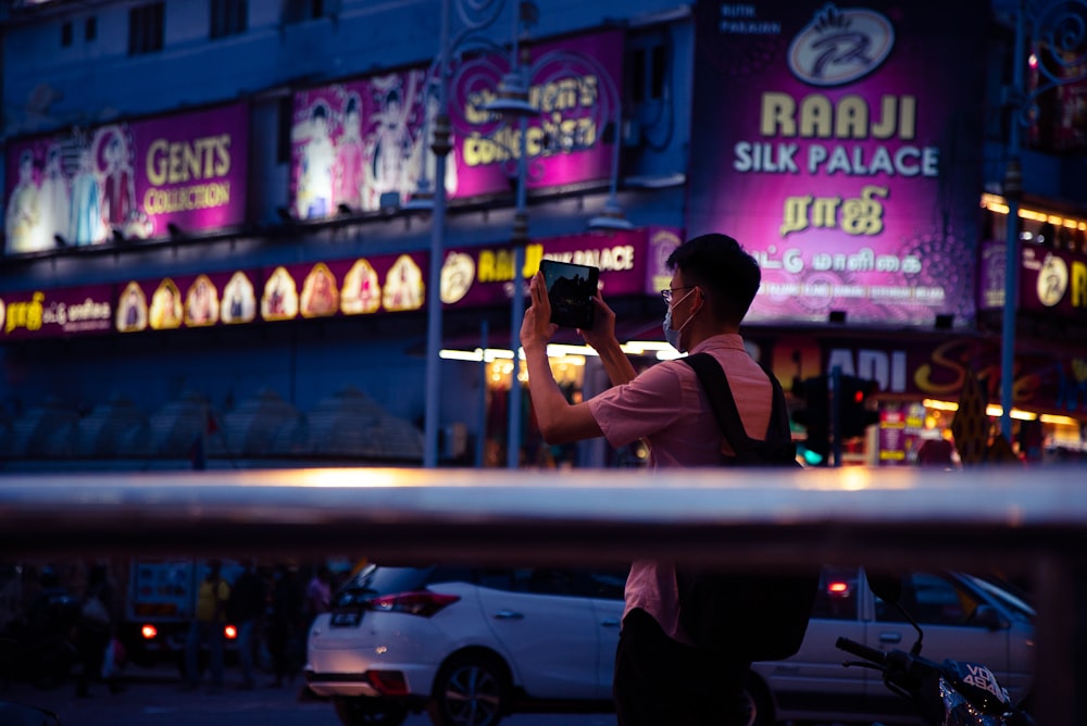 man in white t-shirt taking photo of store during night time
