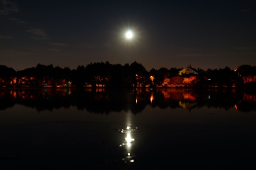 A glowing full moon rising over a tranquil lake, reflecting shimmering light.