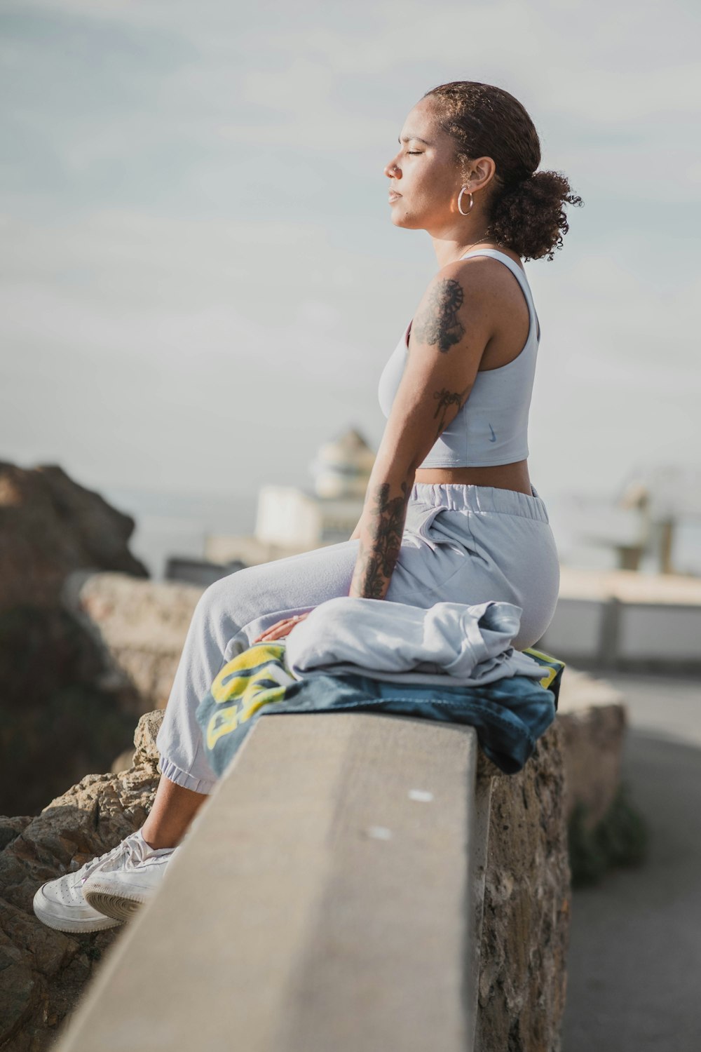 woman in white tank top and white pants sitting on rock during daytime