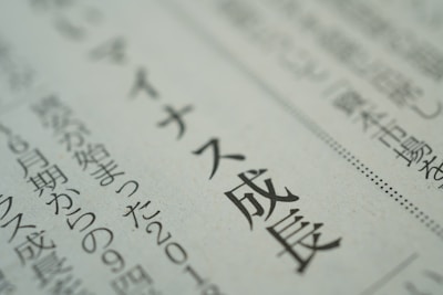 A close-up view of text in Japanese printed on a newspaper or document. The focus is sharp on a section of the text, while the background is blurred, emphasizing the selected words.