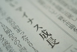 A close-up view of text in Japanese printed on a newspaper or document. The focus is sharp on a section of the text, while the background is blurred, emphasizing the selected words.