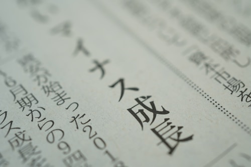 A close-up view of text in Japanese printed on a newspaper or document. The focus is sharp on a section of the text, while the background is blurred, emphasizing the selected words.