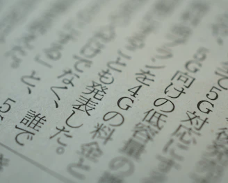 Close-up view of a printed page with Japanese text, displaying several lines of characters in a serif font. The text is slightly blurred, suggesting a shallow depth of field. The paper appears to be off-white in color.