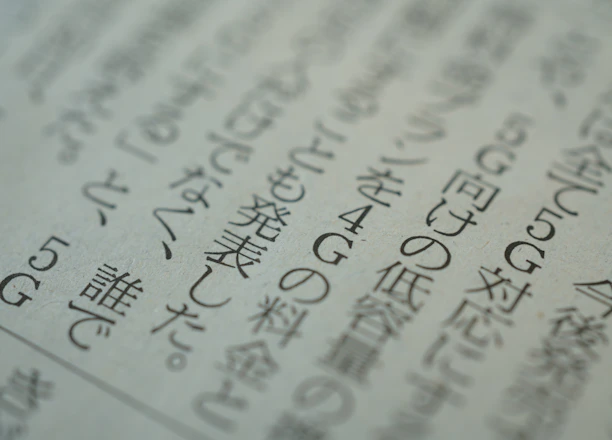 Close-up view of a printed page with Japanese text, displaying several lines of characters in a serif font. The text is slightly blurred, suggesting a shallow depth of field. The paper appears to be off-white in color.