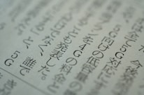 Close-up view of a printed page with Japanese text, displaying several lines of characters in a serif font. The text is slightly blurred, suggesting a shallow depth of field. The paper appears to be off-white in color.