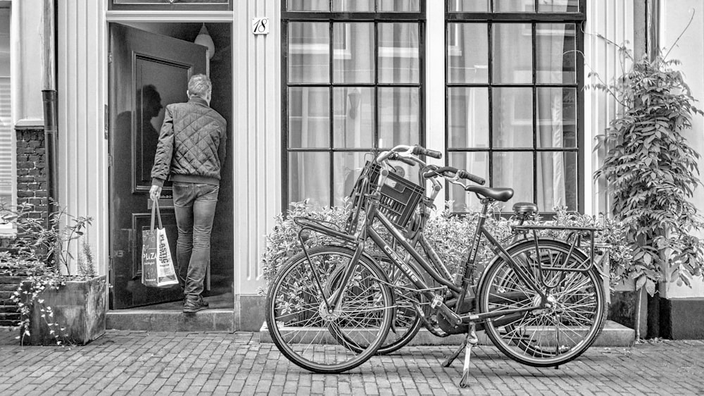 grayscale photo of man in suit standing beside bicycle